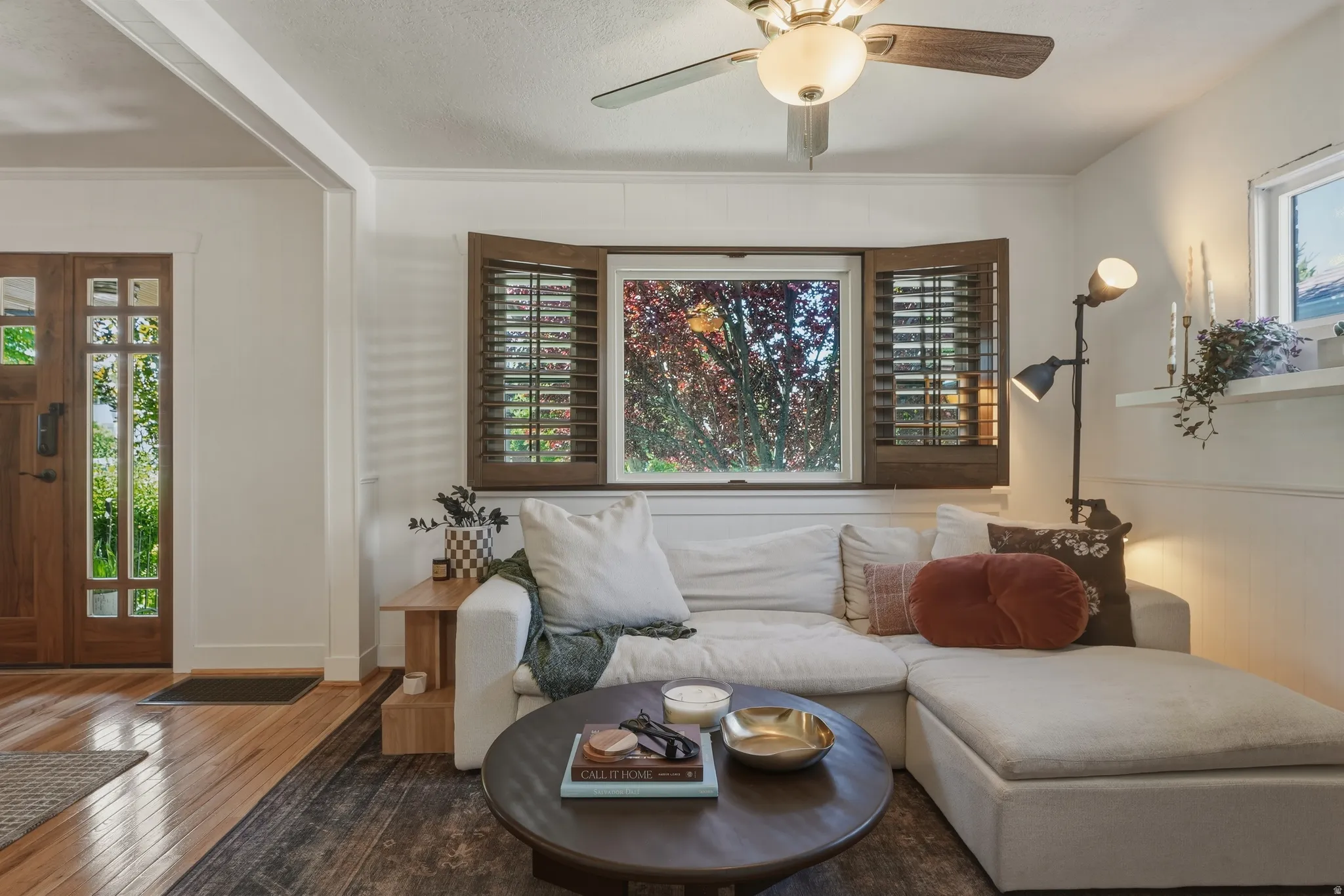 Bright living space featuring a ceiling fan with integrated lighting, wood plantation shutters, and a multi-paned wood entry door