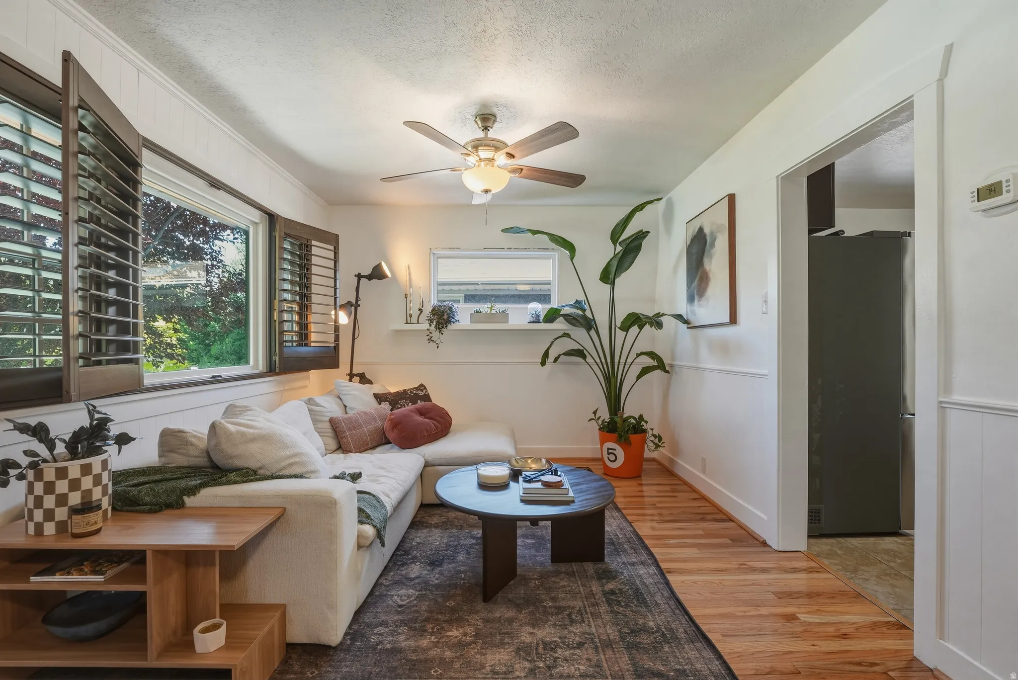 Living area featuring a ceiling fan, wood-finish flooring, decorative wall paneling, and an arched doorway