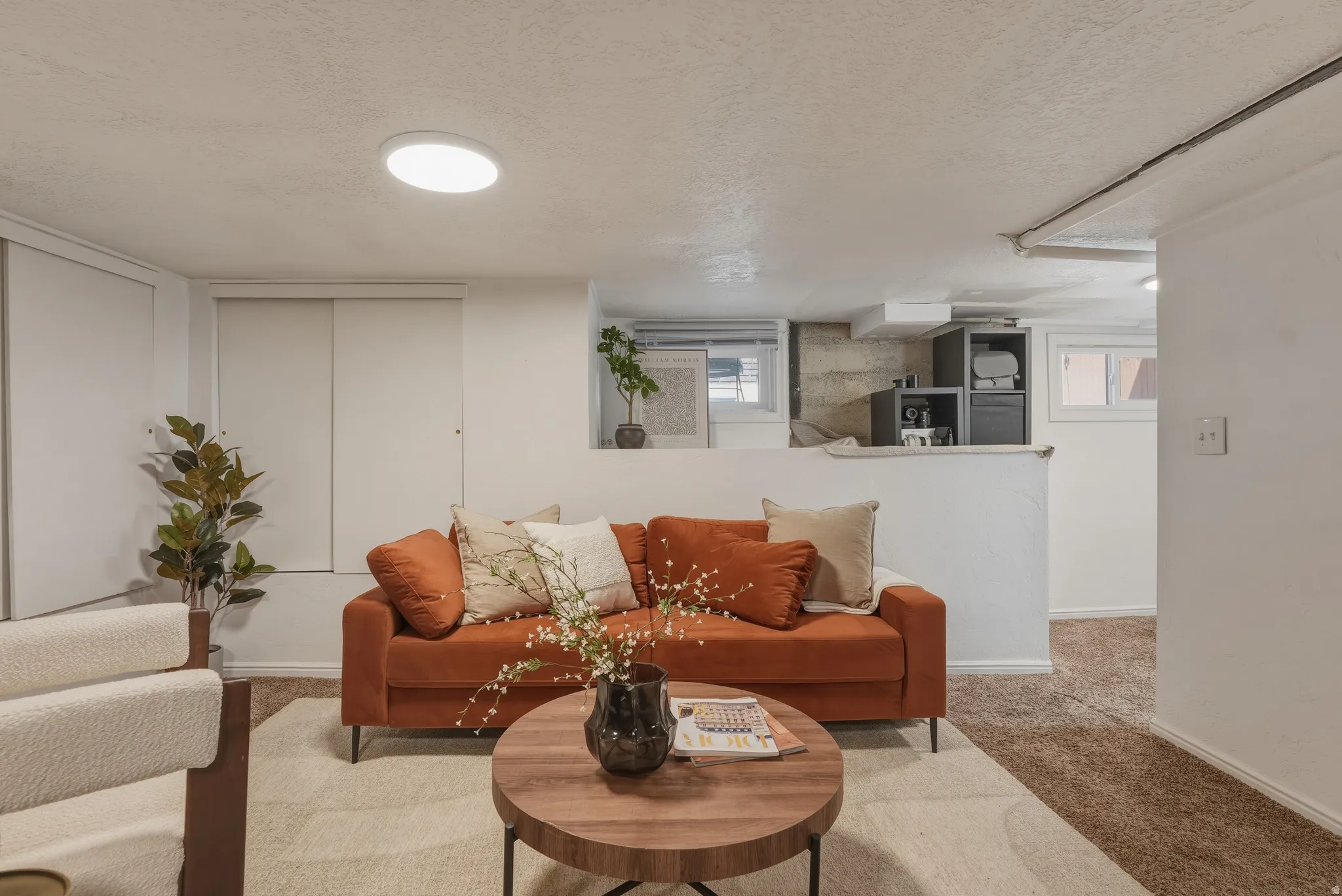Recessed ceiling light fixture illuminating an open-concept living space with white walls and soft brown carpeting
