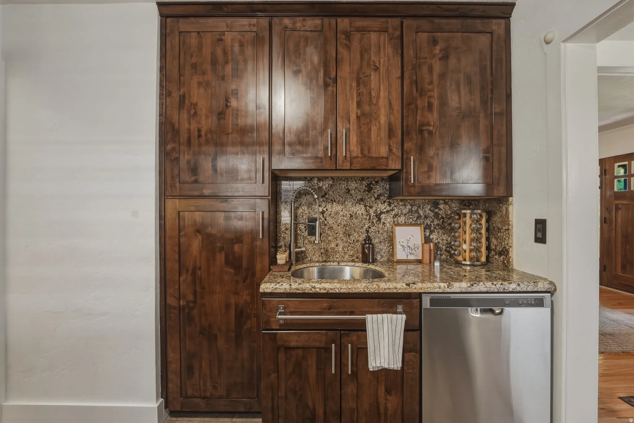 Custom dark wood-finish cabinetry featuring a built-in stainless steel dishwasher, undermount sink, and granite countertops