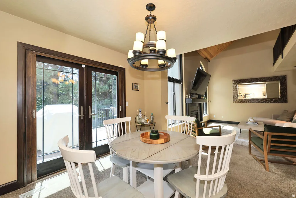 Dining area with a multi-tiered chandelier and wood-finish French doors opening to an exterior deck