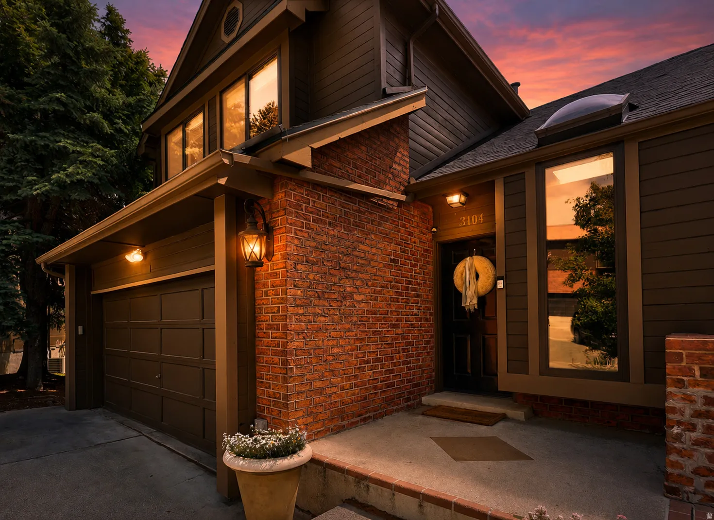 Brick and horizontal siding exterior featuring an attached two-car garage, prominent front door with overhead lighting, and large windows