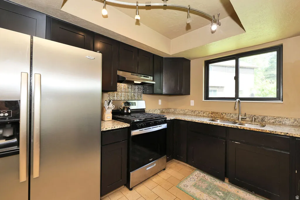 Kitchen featuring dark cabinetry, stainless steel appliances, granite-style countertops, and a tile backsplash