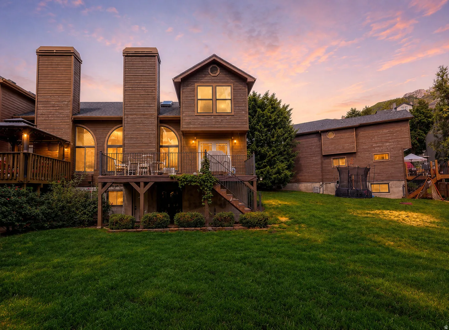Rear exterior featuring a spacious lawn, multiple elevated decks, a wood-sided facade, and arched windows