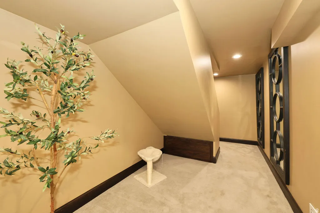 Recessed lighting illuminates a carpeted hallway with dark baseboards and warm-toned walls