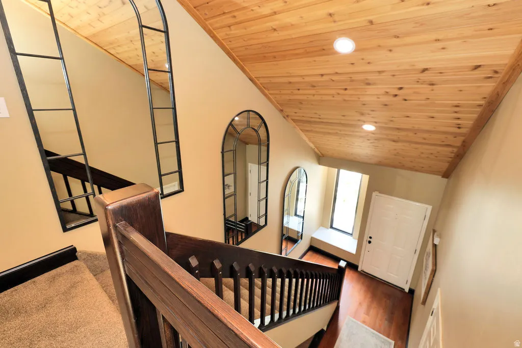 Staircase featuring dark wood-finish banister and carpeted treads, complemented by a wood-paneled ceiling with recessed lighting