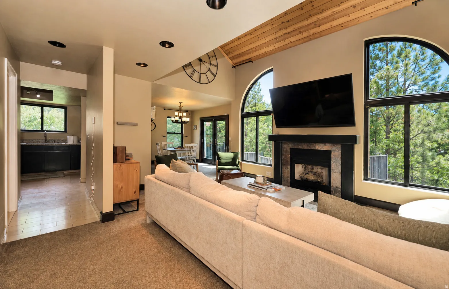 Living area featuring a stone-surround fireplace with a dark mantel, vaulted wood-plank ceiling, recessed lighting, and expansive arched windows