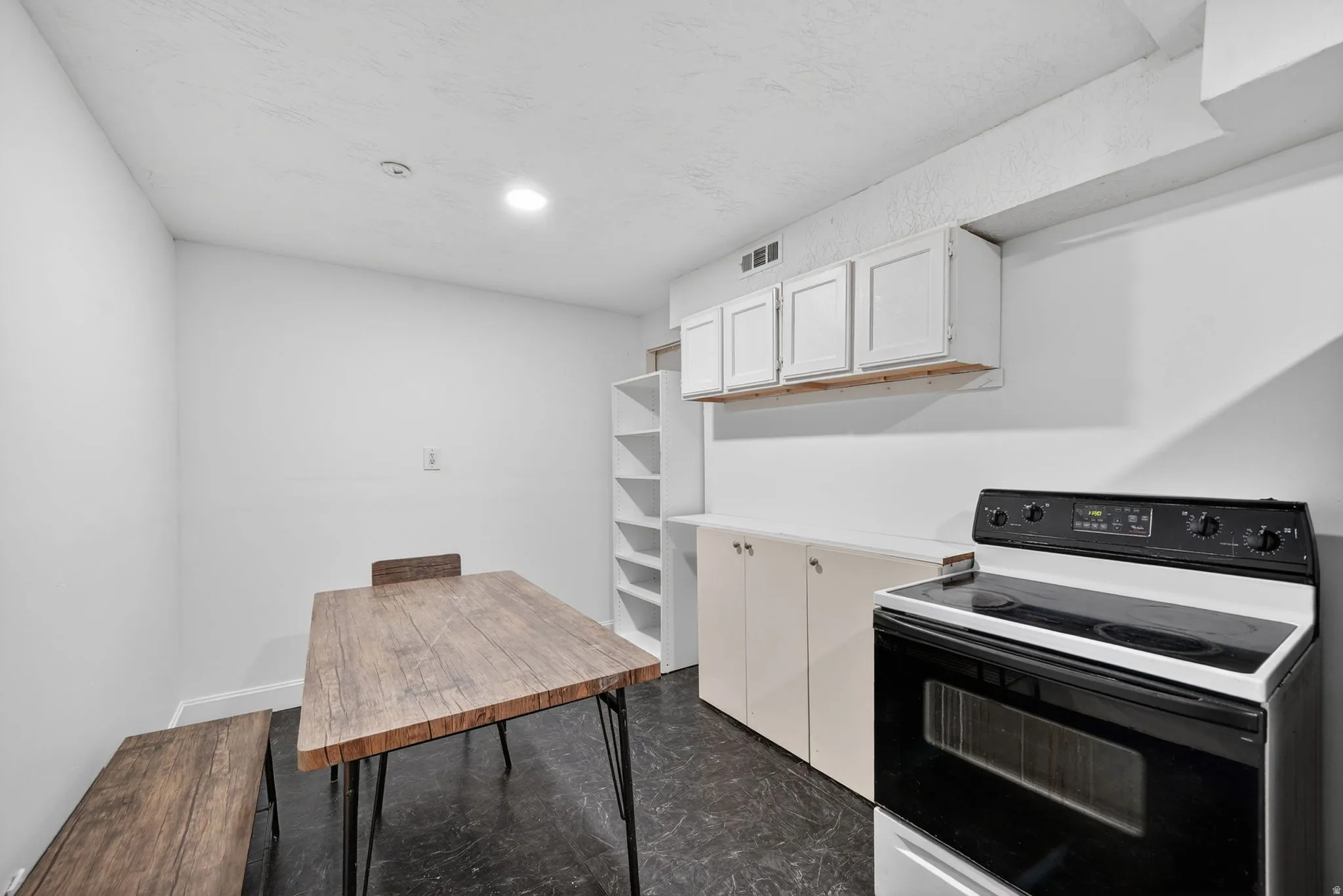 Compact kitchen space featuring a built-in electric range, white upper and base cabinetry, and recessed lighting