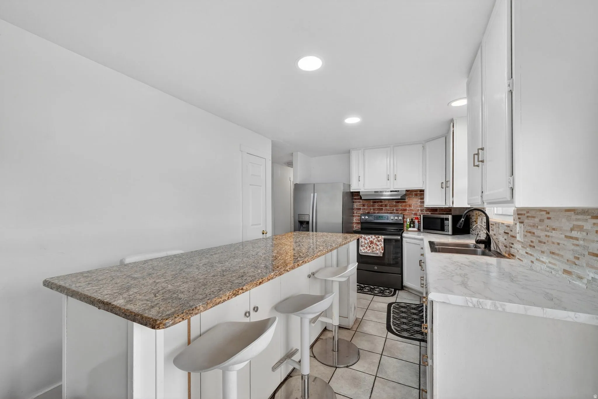 Kitchen featuring an expansive breakfast bar with a speckled countertop, white cabinetry, a brick-style backsplash, stainless steel refrigerator, and recessed lighting