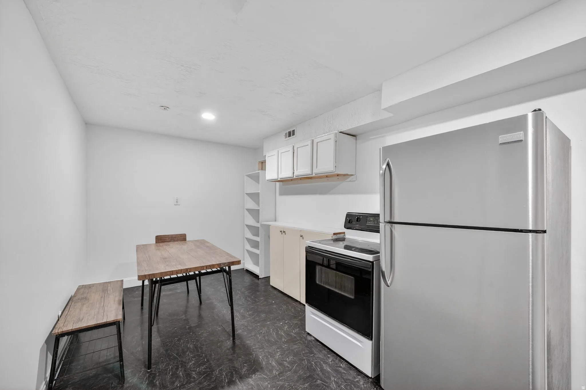Compact kitchen area featuring a stainless steel refrigerator, white electric range, and light-toned upper cabinetry