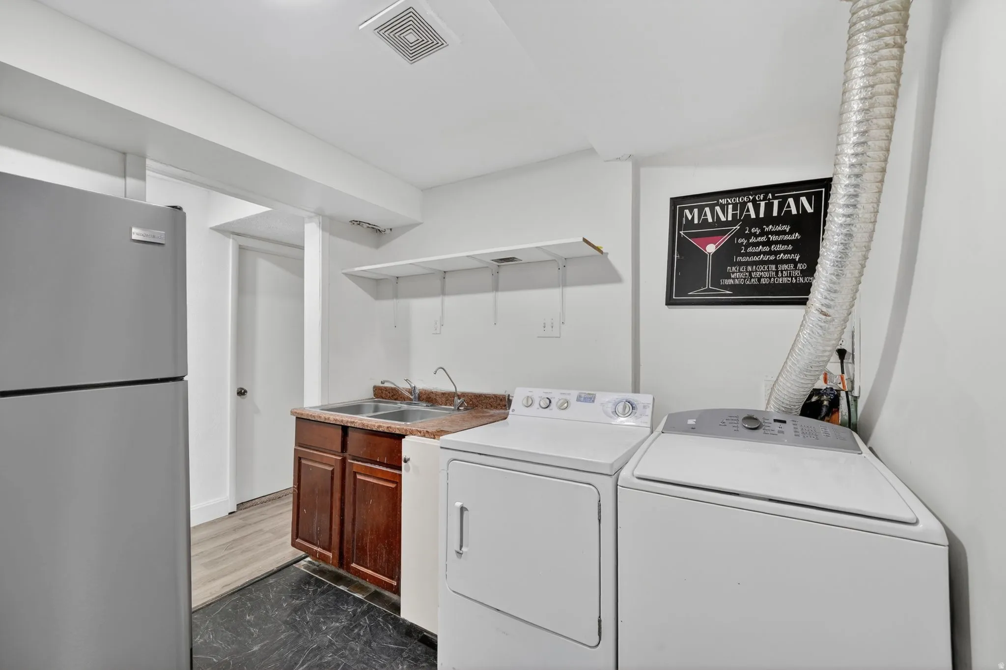 Dedicated laundry area featuring a dual-basin sink with a brown wooden vanity, laminate countertop, and overhead shelving