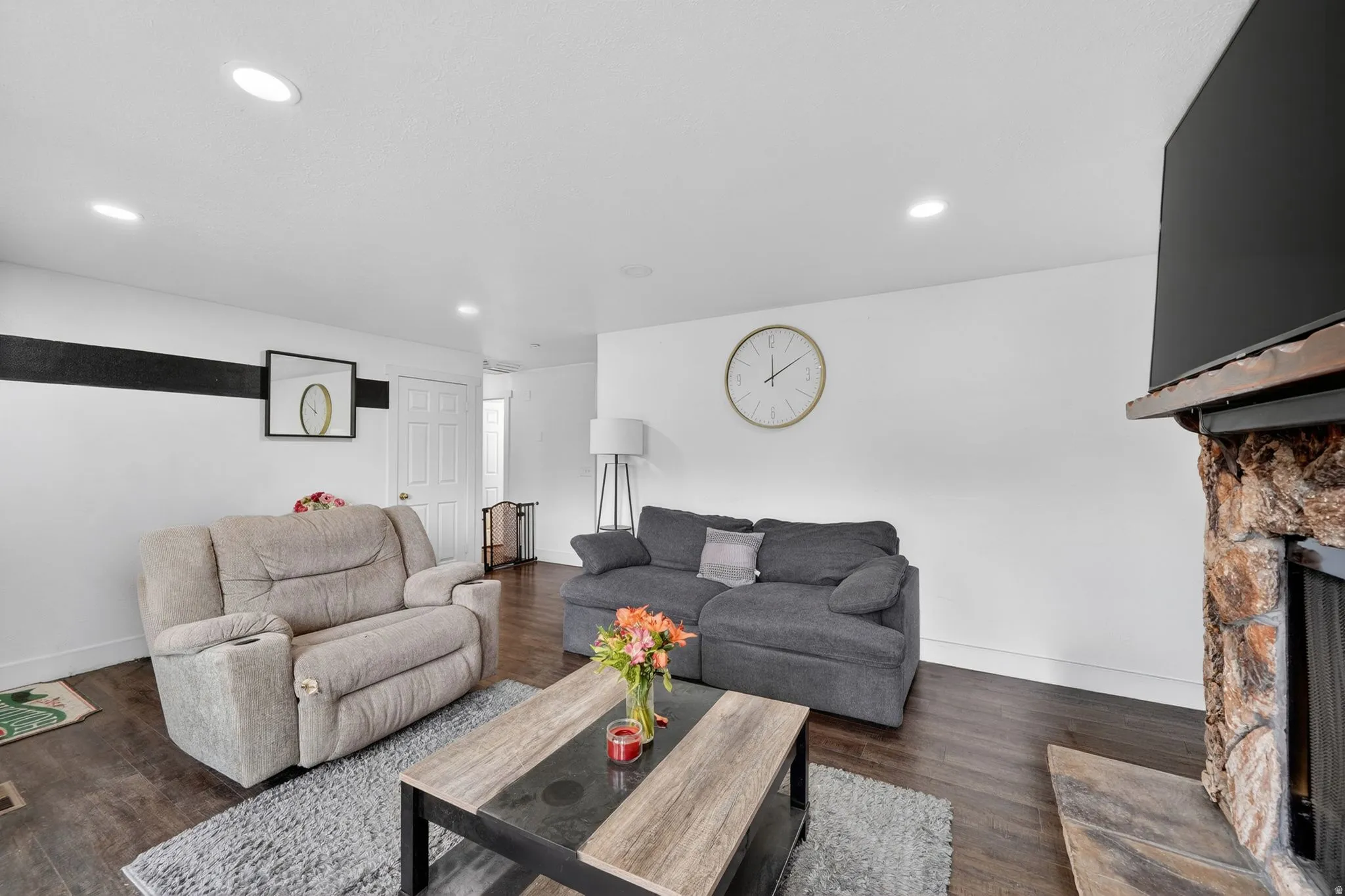 Spacious living area featuring wood-finish flooring, recessed lighting, and a prominent stone fireplace with a wood mantle