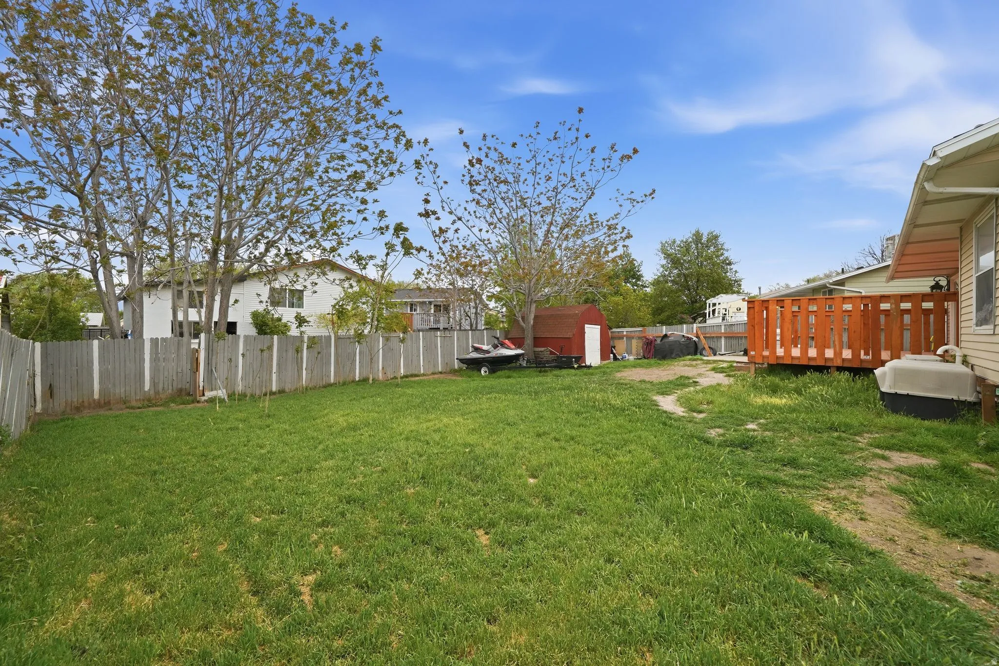 Expansive grassy yard with a wooden privacy fence, mature trees, a red storage shed, and a wooden deck structure
