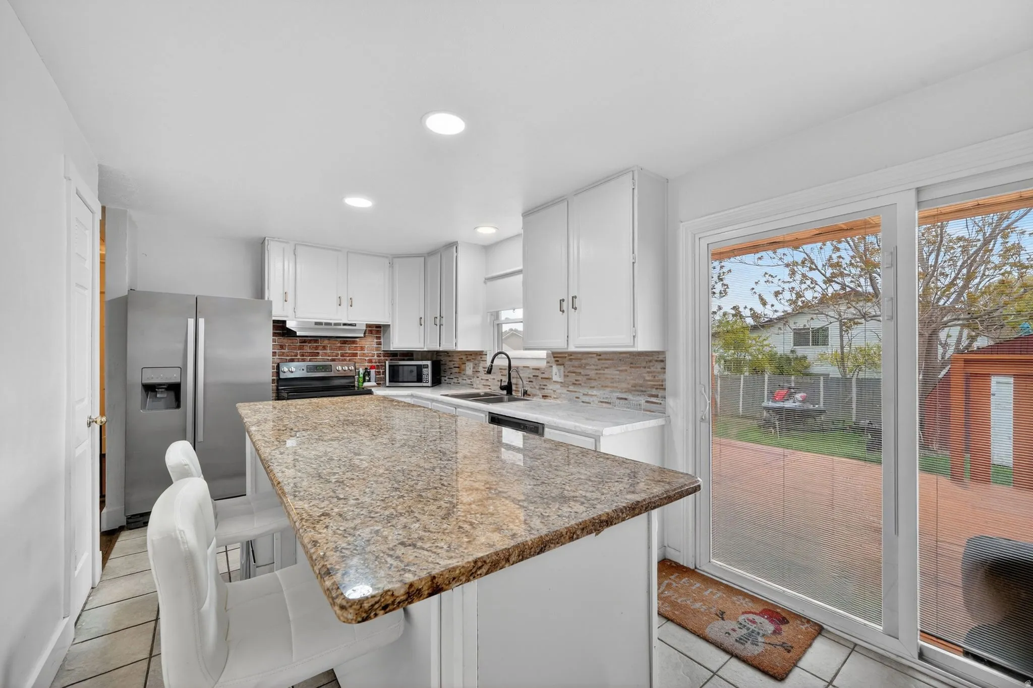 Kitchen featuring white cabinetry, a large center island with a speckled countertop, and a brick-look tile backsplash