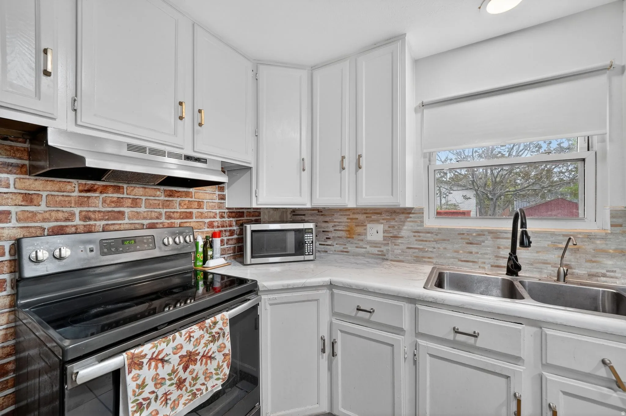 Kitchen featuring white cabinetry, a black electric range, a stainless steel double basin sink with a black faucet, and a tiled backsplash