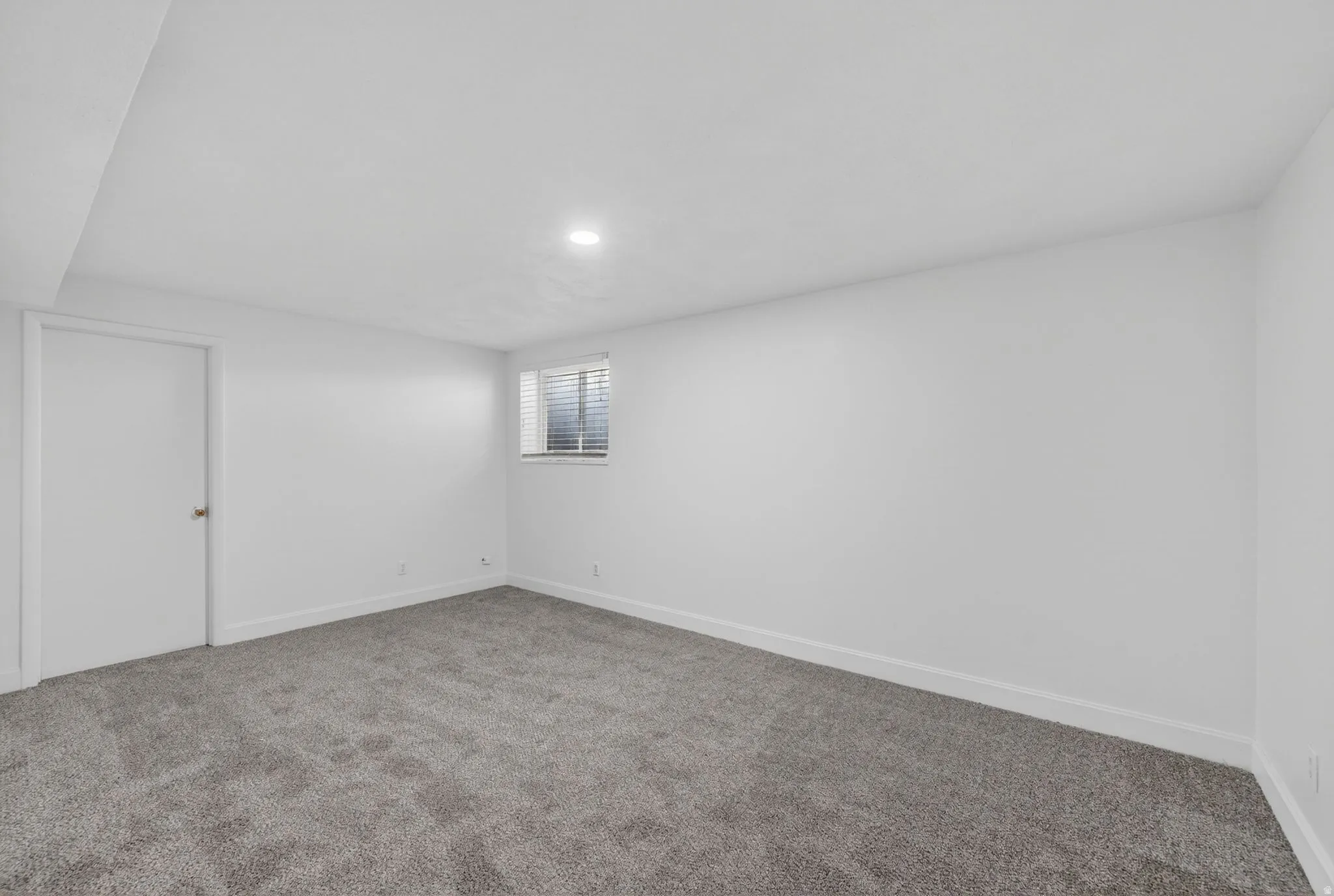 Carpeted room featuring a single window with horizontal blinds, white walls, and a recessed ceiling light