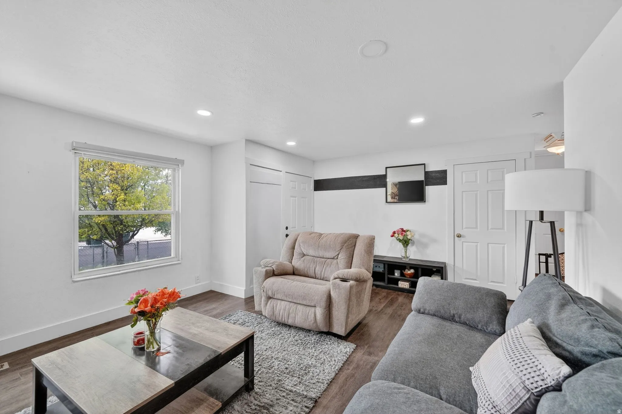 Living area featuring wood-finish flooring, white walls, recessed lighting, and a window with a tree view