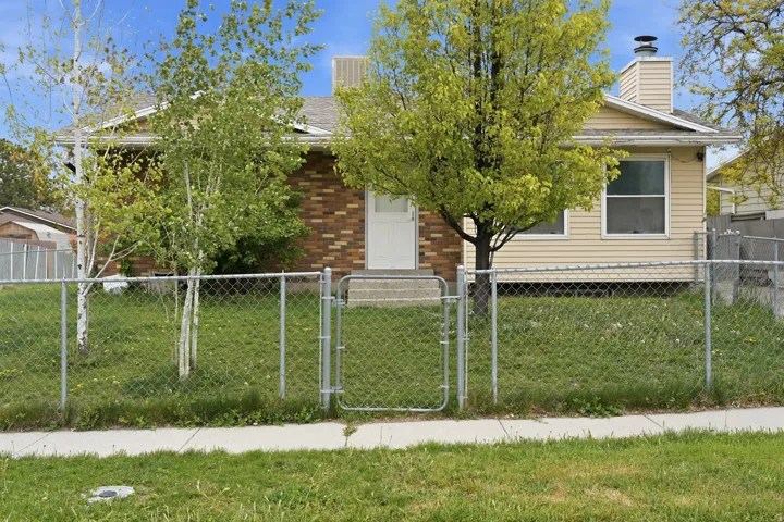 Exterior featuring a brick and siding facade, a fenced front yard with mature trees, and a concrete sidewalk
