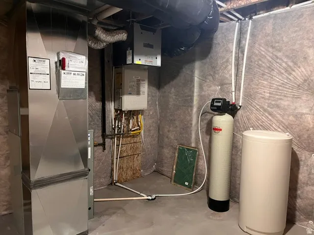Utility area featuring exposed joist ceiling, concrete flooring, insulated ductwork, a water softener, and a water heater
