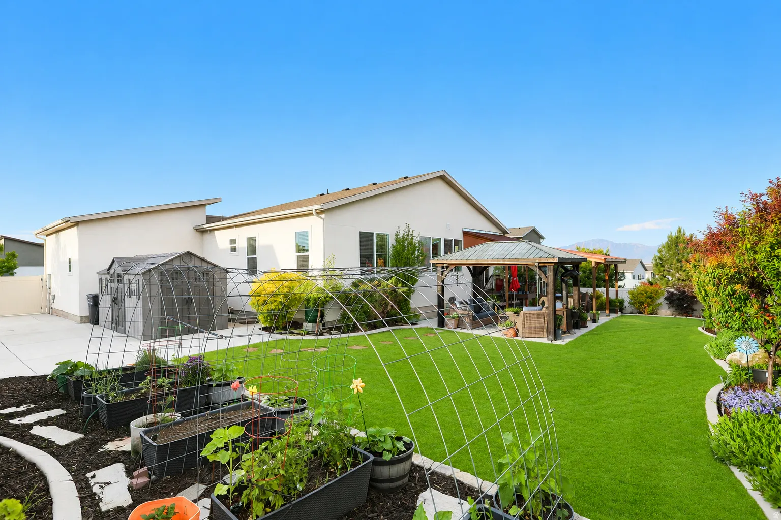Expansive backyard featuring a lush lawn, raised garden beds, and a covered patio structure