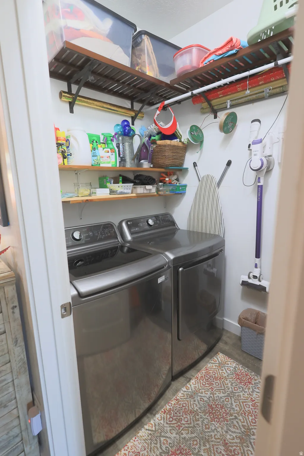 Dedicated utility space on first level, featuring a top-load washer and dryer set, waterproof luxury vinyl plank flooring, and multiple wall-mounted shelving units