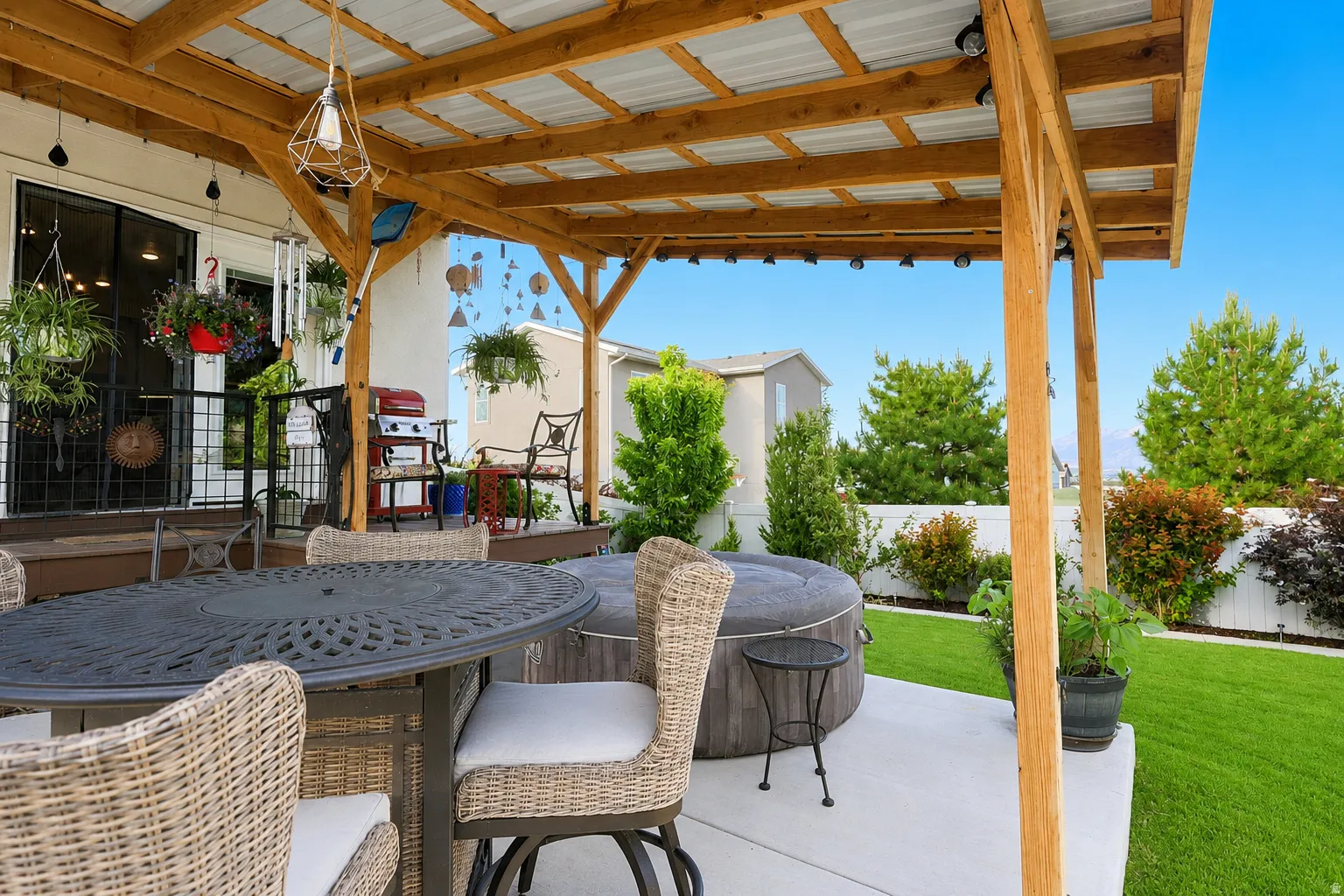 Outdoor covered patio featuring a wood-beam pergola with a corrugated metal roof, integrated string lighting, and a concrete patio slab