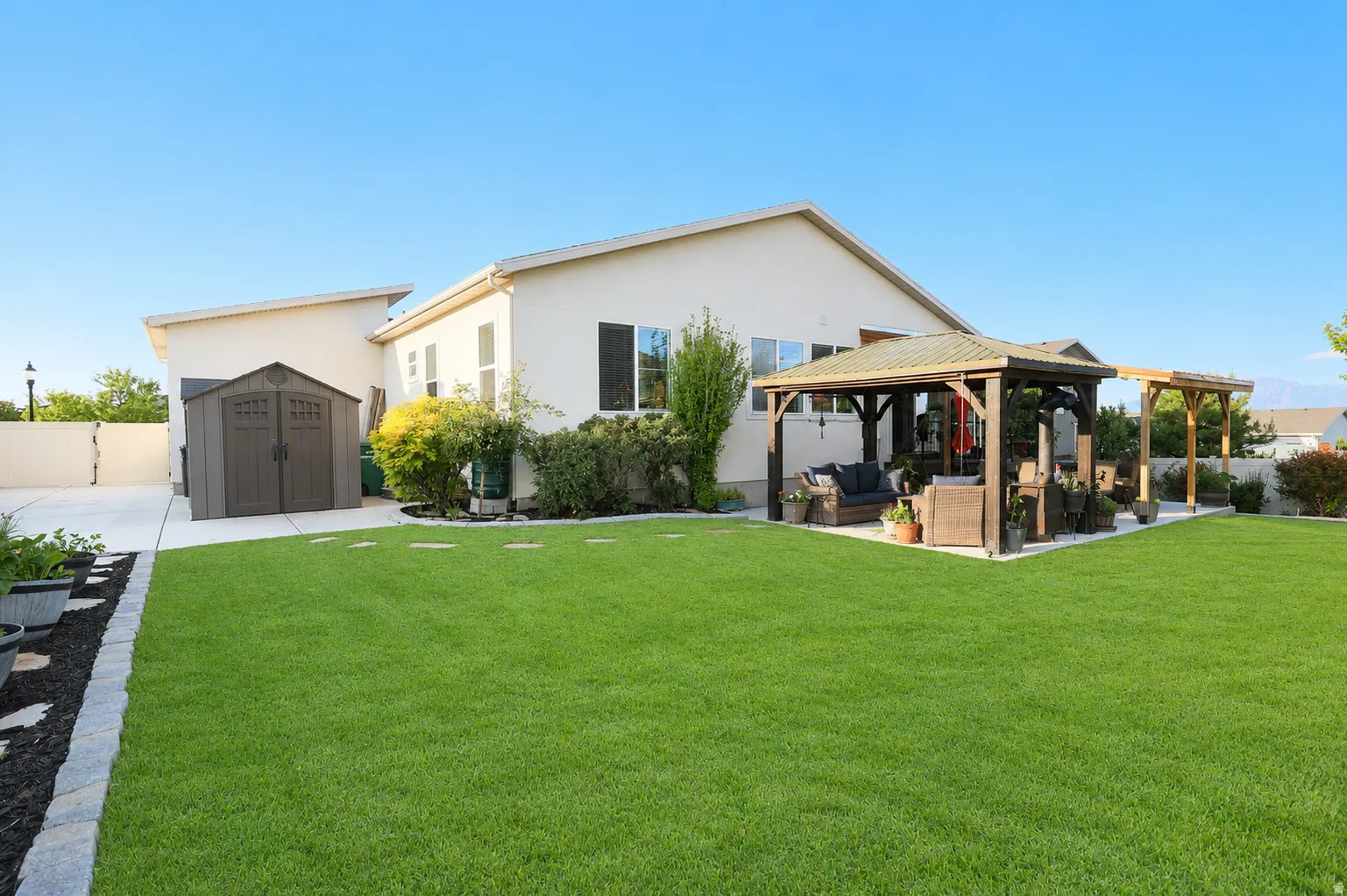 Expansive lawn with a paver border, leading to a concrete patio featuring a wood gazebo and an additional wood pergola