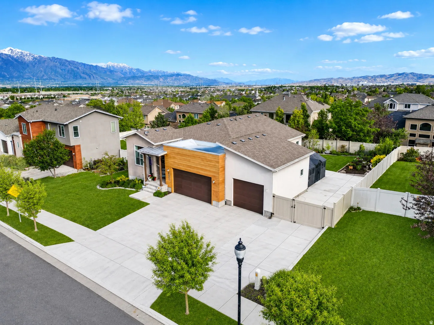 Contemporary residence featuring a three-car garage with wood-finish door, extensive concrete driveway, and front porch with wood-finish accents