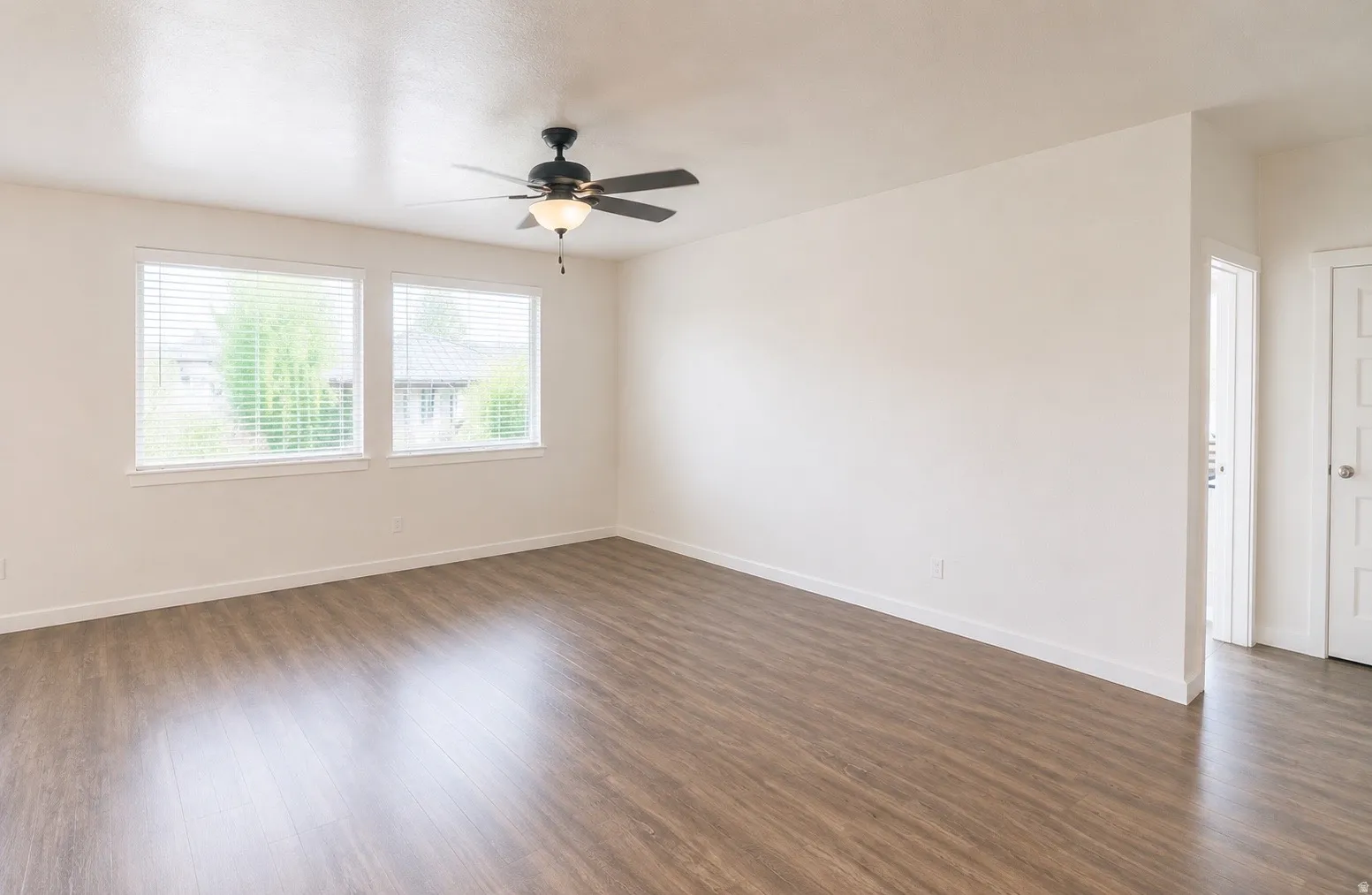 Spacious living area featuring waterproof luxury vinyl plank flooring, a ceiling fan with integrated lighting, and multiple large windows for all the natural light