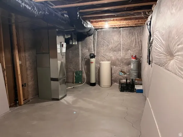 Utility area featuring exposed joist ceiling, concrete flooring, insulated ductwork, a water softener, and a water heater