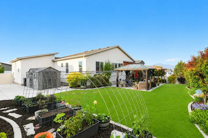 Expansive backyard featuring a lush lawn, raised garden beds, and a covered patio structure