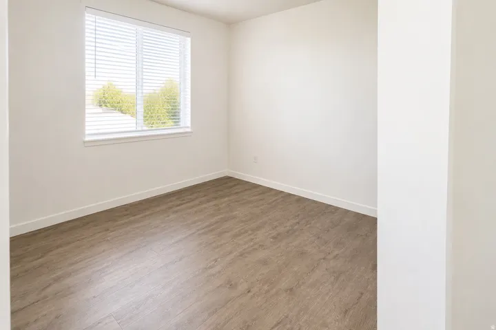 Bright room featuring a large window with white blinds, wood-finish flooring, and light-colored walls