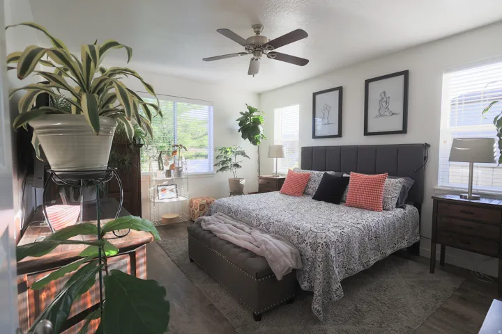 Spacious master bedroom featuring waterproof luxury vinyl plank flooring, a ceiling fan, and multiple windows with blinds