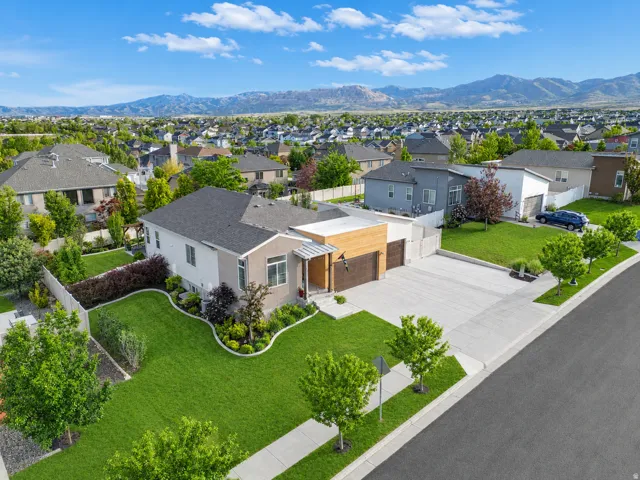 Contemporary residence featuring a three-car garage with wood-finish door, extensive concrete driveway, and front porch with wood-finish accents
