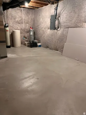 Utility area featuring exposed joist ceiling, concrete flooring, insulated ductwork, a water softener, and a water heater