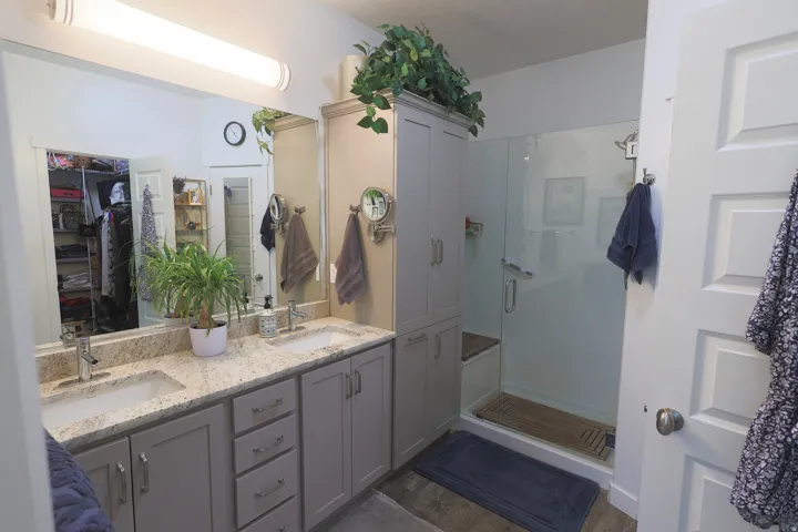 Master Bathroom featuring a dual vanity with light-toned countertops, undermount sinks, walk in glass shower with bench seat.