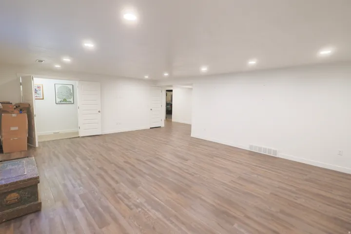 Spacious basement family room featuring waterproof luxury vinyl plank flooring, recessed lighting, white walls, and multiple paneled doors