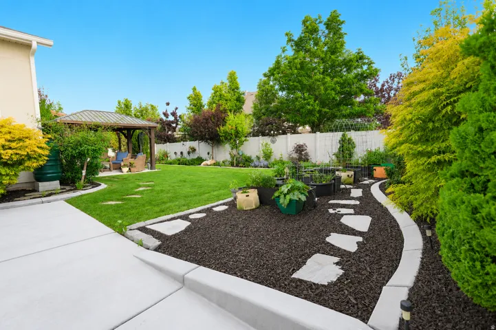 Expansive backyard featuring a lush lawn, a dedicated garden area with stepping stones, a concrete patio, a covered gazebo, and mature landscaping