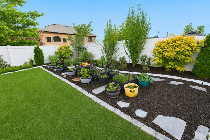 Fenced backyard featuring an lush lawn, a mulched planting area with stone pavers, and mature perimeter trees and shrubs