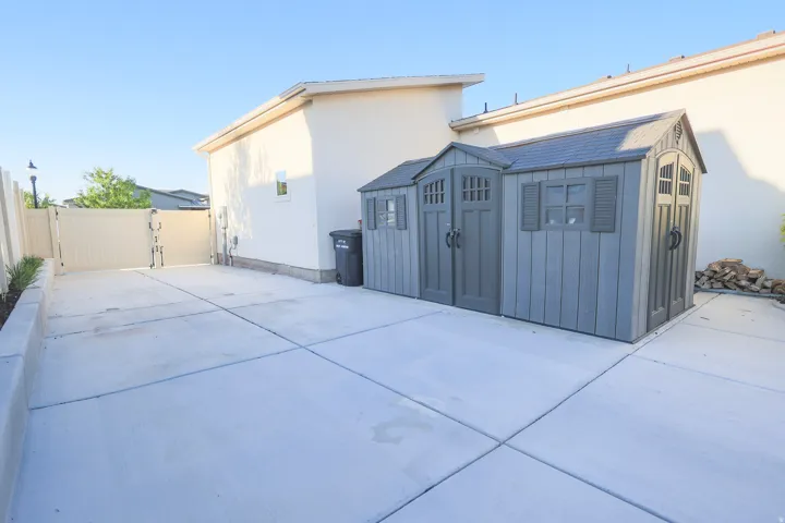 Expansive concrete pad with double gate entrance featuring a grey storage shed with shuttered windows and double doors on two sides