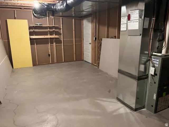 Utility area featuring exposed joist ceiling, concrete flooring, insulated ductwork, a water softener, and a water heater