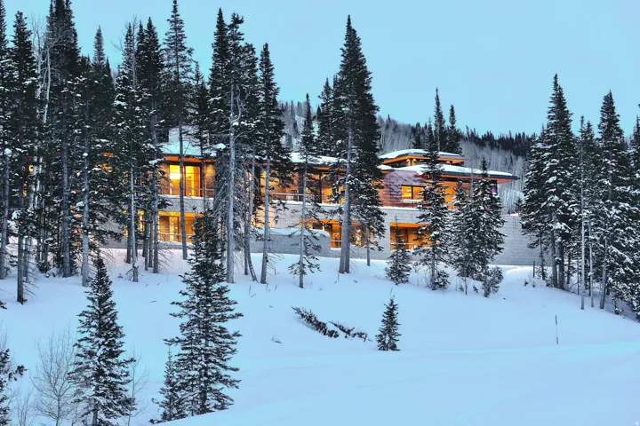Contemporary mountain-style residence featuring extensive glazing, stacked stone exterior elements, and a multi-tiered roofline