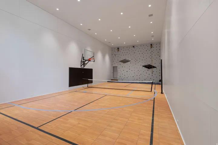 Indoor multi-sport court featuring wood-finish flooring with court markings, a basketball hoop, and a net