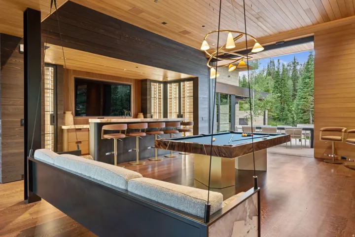 Expansive entertainment space featuring wood-finish flooring, a built-in wet bar with stone countertop, a billiards table, and a suspended swing seat