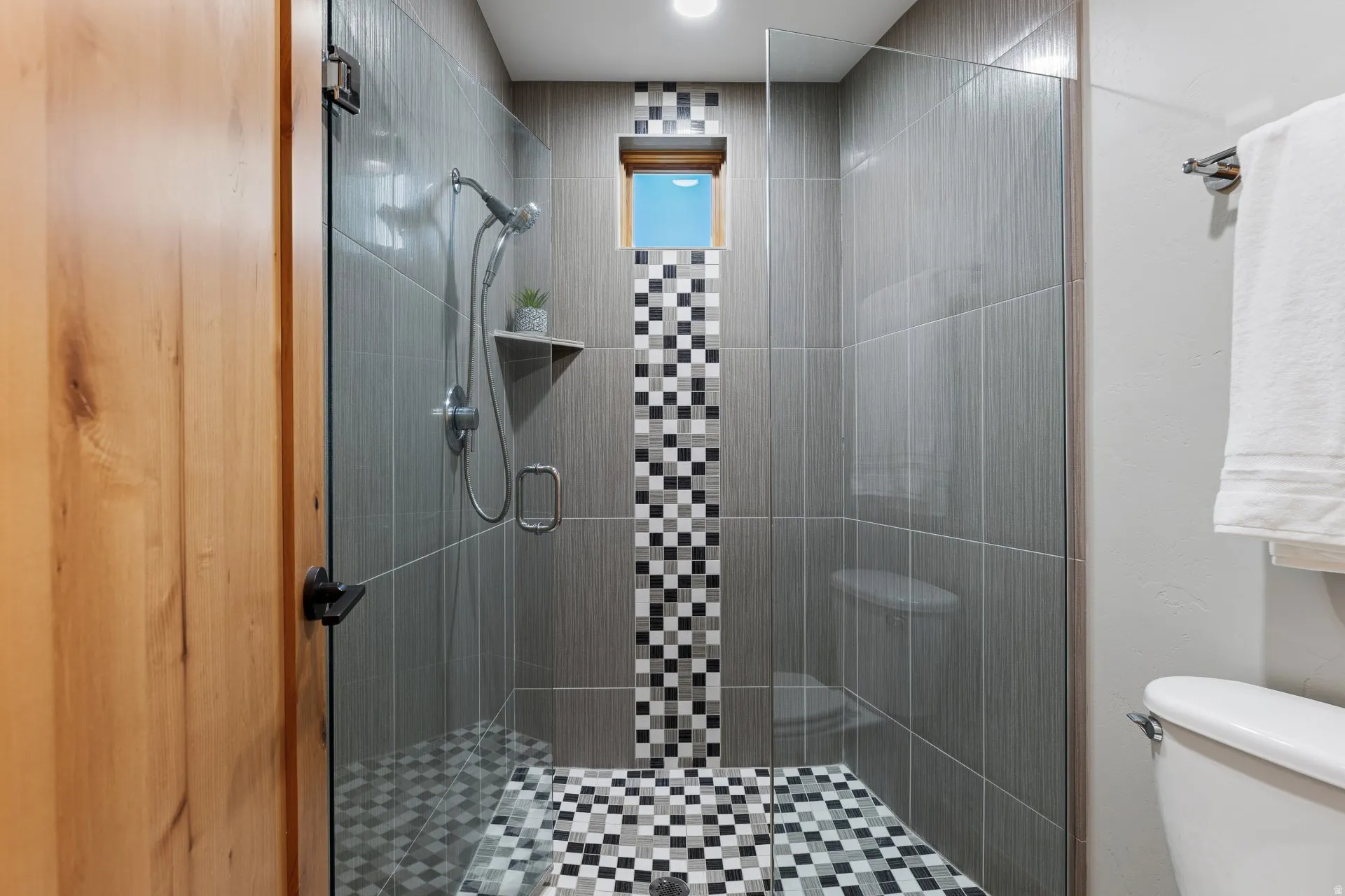 Walk-in shower with clear glass enclosure and black and white mosaic tile flooring