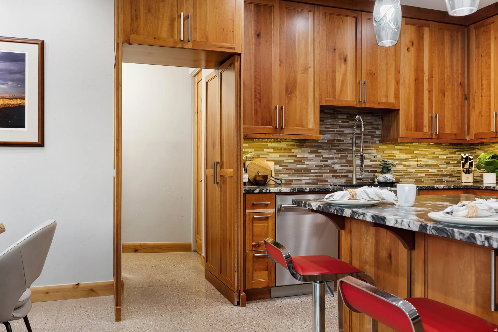 Kitchen featuring wood cabinetry, stainless steel dishwasher, a multi-tone tile backsplash, and a black and white variegated countertop