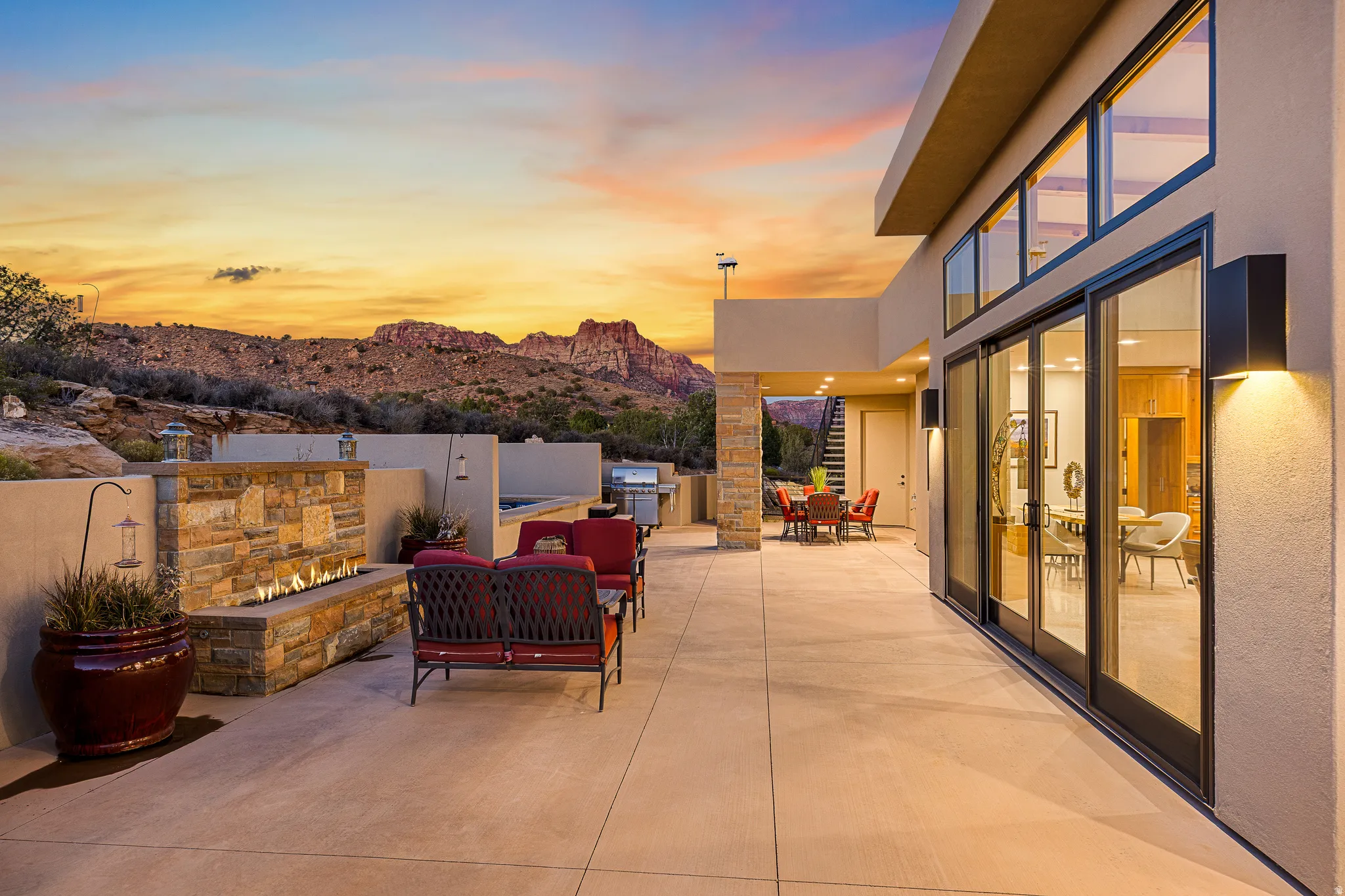 Expansive outdoor patio featuring a stone-clad fireplace and integrated gas fire pit, built-in BBQ station, and a mountain backdrop