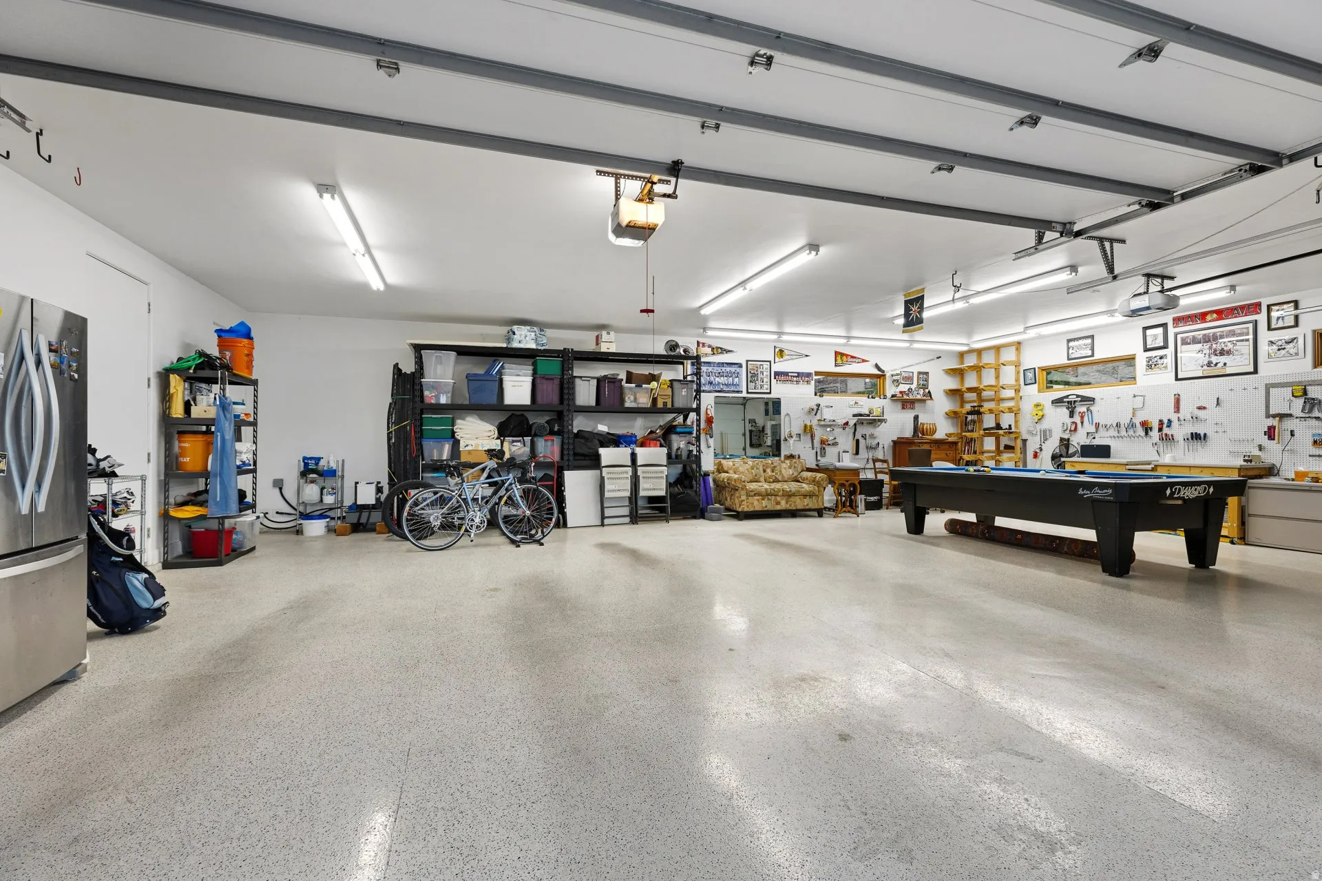 Expansive garage space featuring speckled epoxy flooring, bright overhead fluorescent lighting, and a prominent workbench with shelving