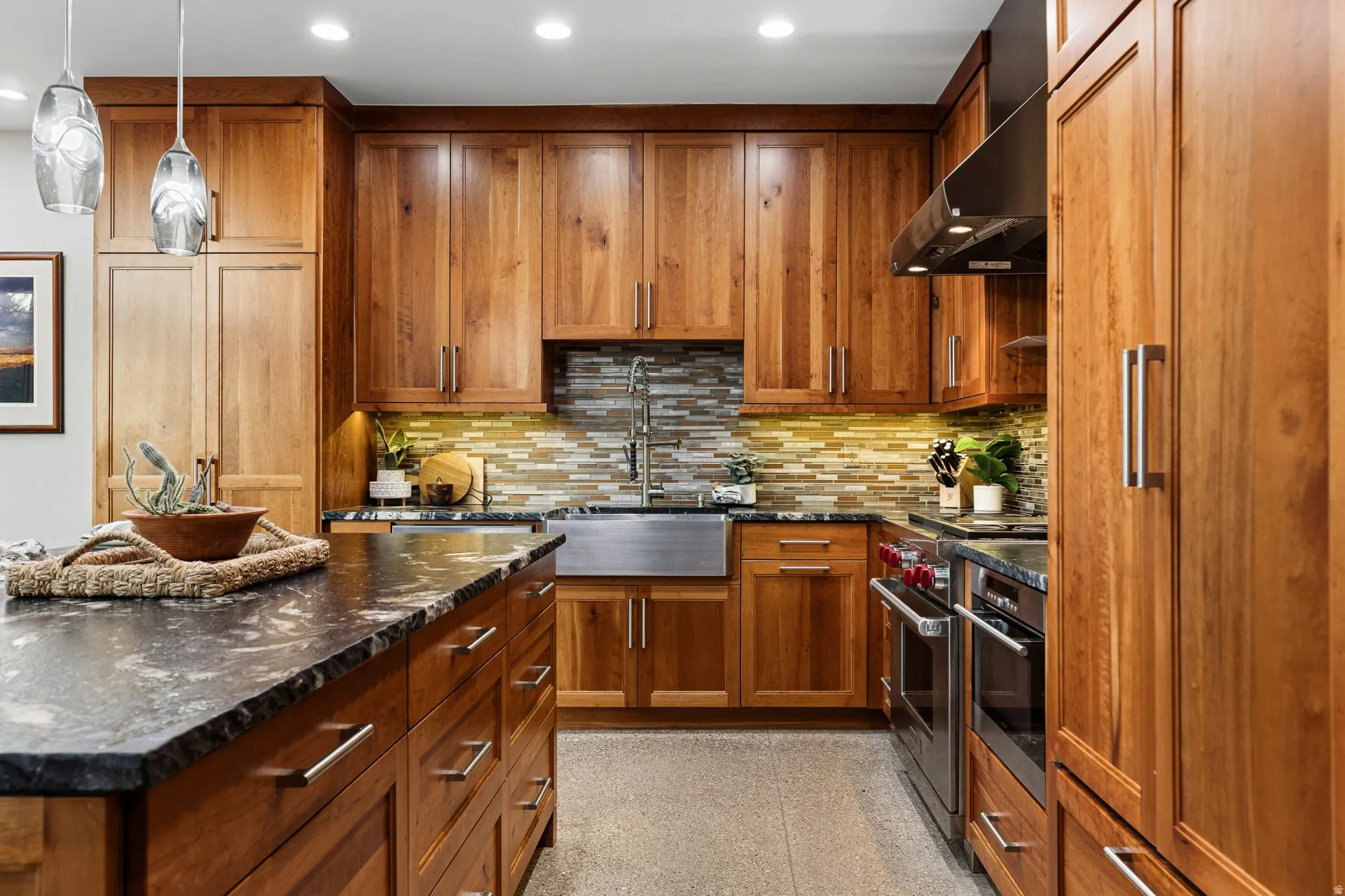 Kitchen featuring extensive wood cabinetry, dark stone countertops, a stainless steel farmhouse sink, a tile backsplash, and recessed lighting