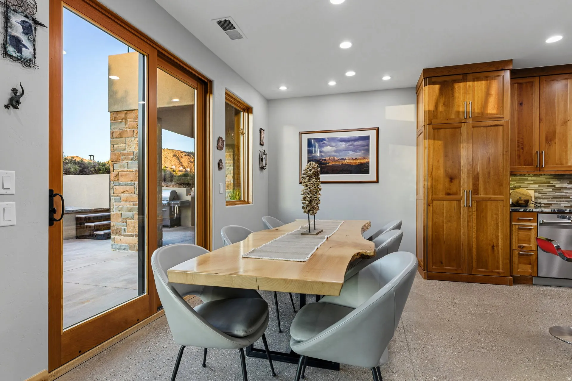Dining area featuring a wood-finish live-edge table, recessed lighting, and access to an outdoor patio with stone cladding